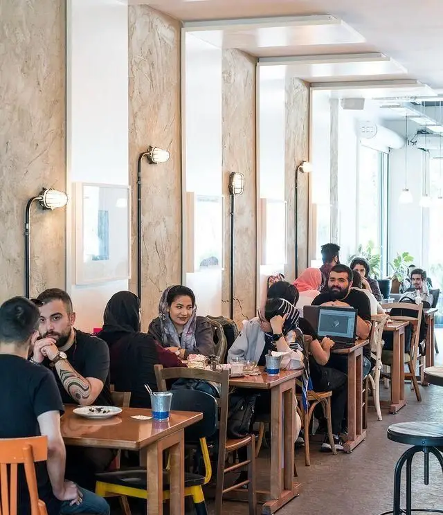 فضای داخلی کافه روبرتو با مشتریانی که در حال دورهمی و کار با لپ‌تاپ هستند، محیطی دلنشین و دوستانه برای قهوه و مطالعه در تهران.