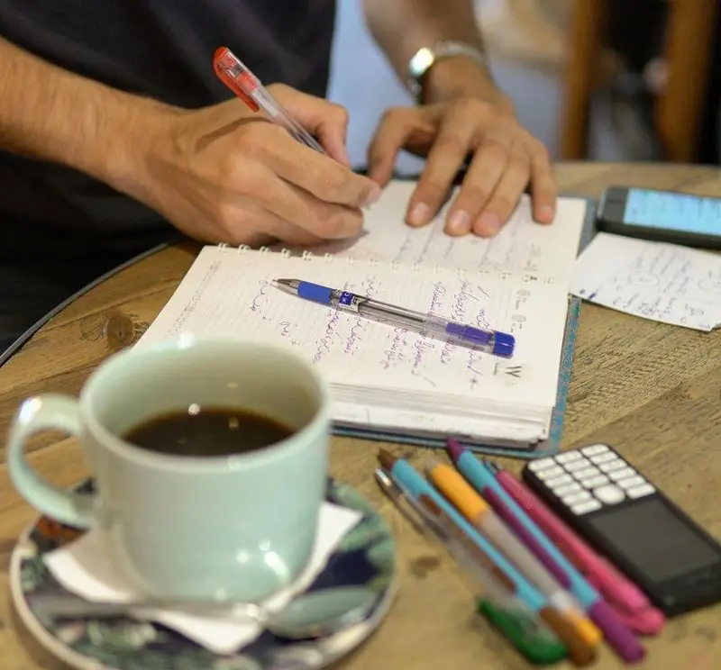 تصویری از مشتری در کافه روبرتو که با قهوه و دفترچه در حال کار و نوشتن است. محیطی آرام و ایده‌آل برای تمرکز و فعالیت‌های فکری.