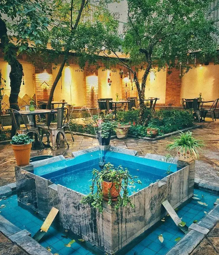 کافه مانا: حیاطی دنج و سرسبز با فواره آبی دلنشین، میز و صندلی‌های فلزی مدرن و نورپردازی گرم. فضایی عالی برای آرامش.