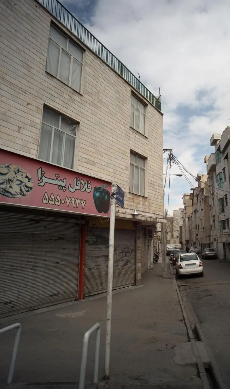 تصویری از نمای یک خیابان در شهر با کسب و کار فلافل پیتزا، تابلوی قرمز با نماد فلفل دلمه‌ای، کرکره‌های پایین و شماره تلفن ۵۵۵-۷۹۳۷.