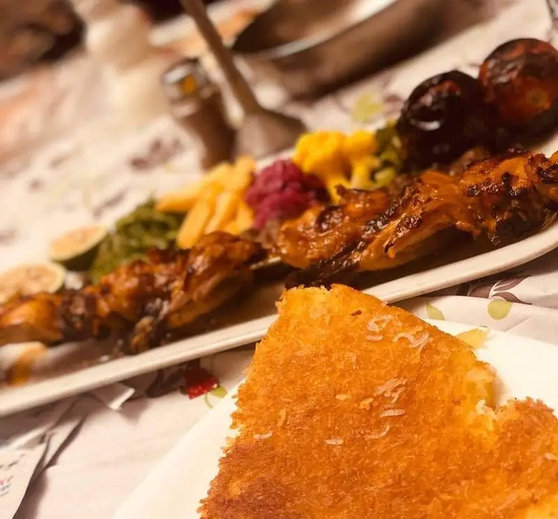 نمایی از جوجه کباب آبدار رستوران ماه و مهر به همراه ته دیگ برشته و دورچین‌های رنگارنگ. غذای سنتی ایرانی برای یک وعده عالی.