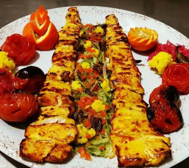 کباب جوجه زعفرانی آبدار رستوران ماه و مهر، با سس مخصوص و دورچین سالاد تازه، گوجه کبابی و میوه‌آرایی زیبا؛ غذای سنتی ایرانی.