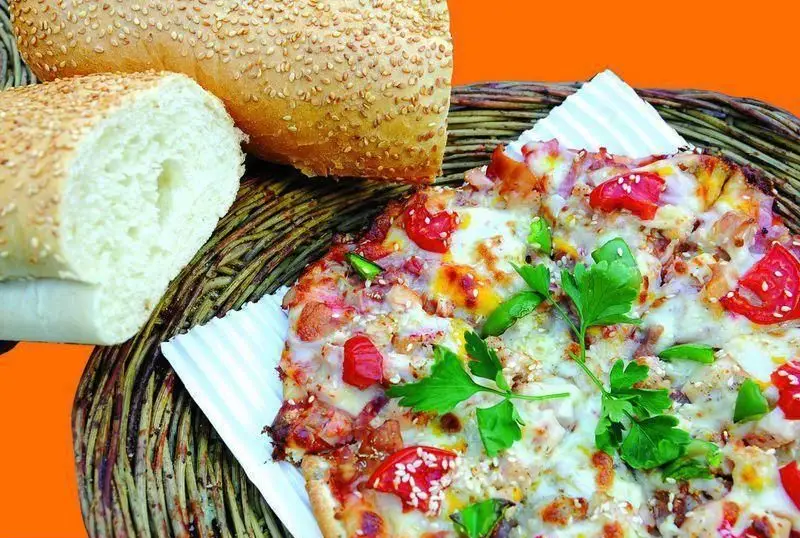 پیتزا آلونک خوشمزه با پنیر ذوب شده، تکه های مرغ، فلفل دلمه و گوجه فرنگی، در کنار نان کنجدی تازه روی سبد حصیری