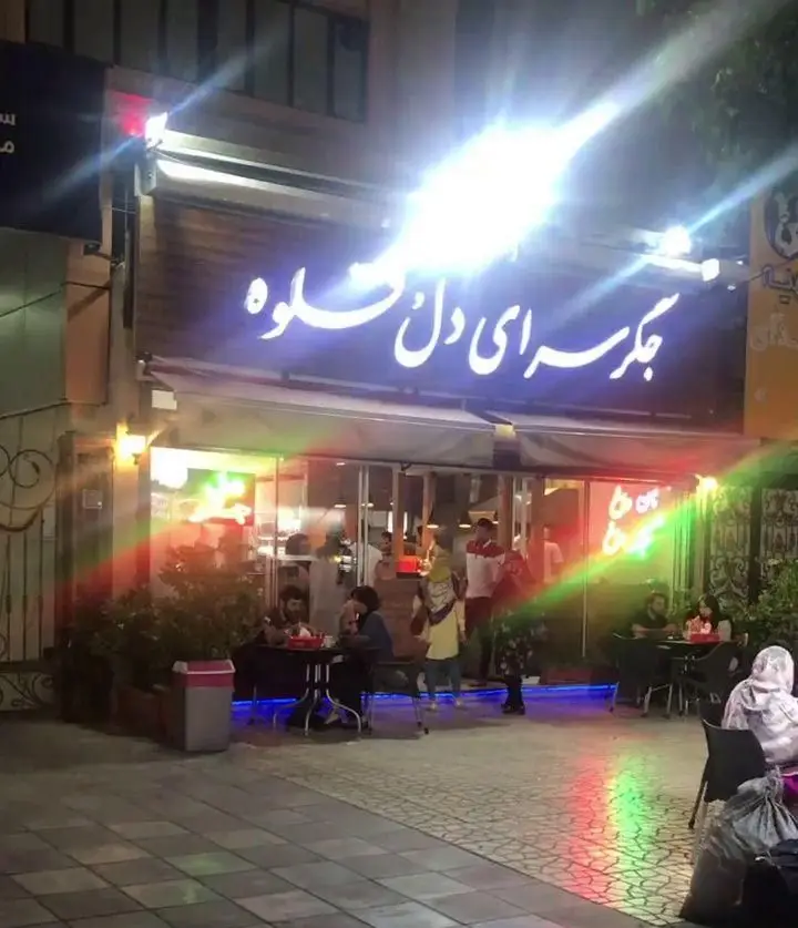 تصویری از نمای بیرونی جگر سرای دل و قلوه در شب، با تابلوی نئونی درخشان و میزهای چیده شده در فضای باز برای مشتریان.