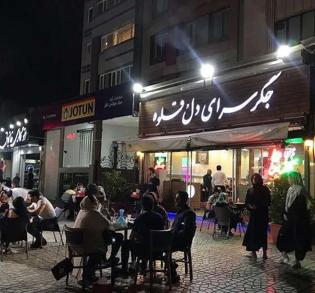 نمایی از جگر سرای دل و قلوه در شب با مشتریانی که در فضای باز مشغول صرف انواع کباب و جگر تازه هستند.