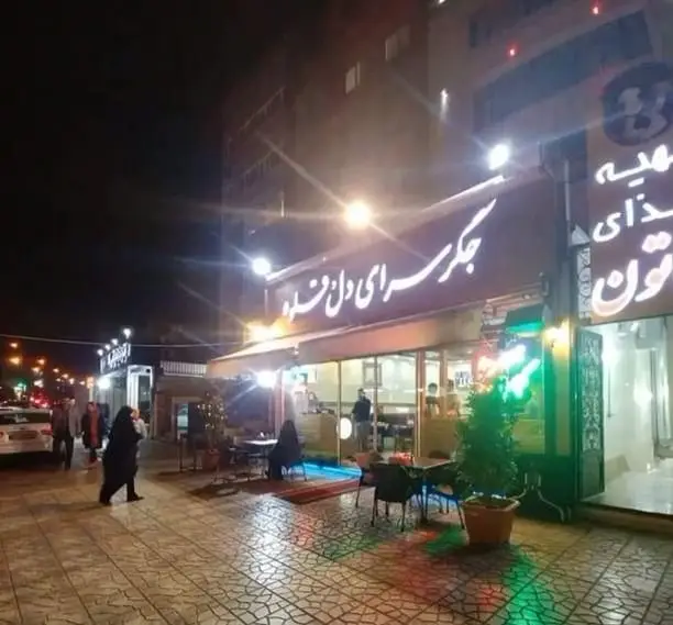 نمای شبانه پرجنب‌وجوش از رستوران جگر سرای دل و قلوه، با تابلوهای نئونی درخشان و مشتریانی که از فضای دلنشین و غذای لذیذ لذت می‌برند.