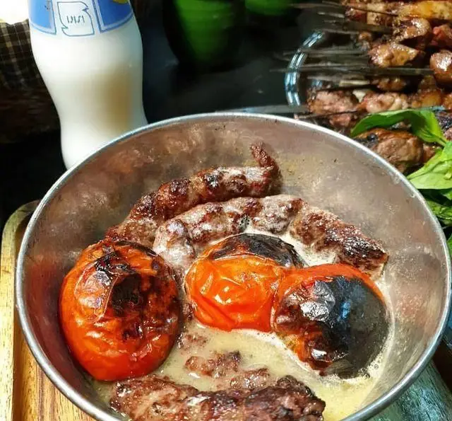 کباب‌های آبدار و داغ جگر، دل و قلوه با گوجه‌فرنگی‌های کبابی و سس لذیذ در ظرف فلزی. غذای اصیل جگر سرای دل و قلوه با دوغ.