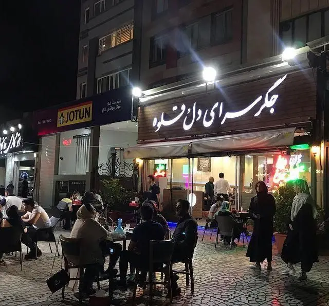 تصویر شب از جگر سرای دل و قلوه با فضای باز پر از مشتریان مشغول صرف کباب جگر، دل و قلوه و نوشیدنی، محیطی دلنشین.