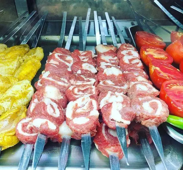 تصویری از سیخ‌های کباب گوشت و مرغ تازه در کنار گوجه‌های نصف شده آماده گریل در جگرسرای دل و قلوه، آماده برای مشتریان.