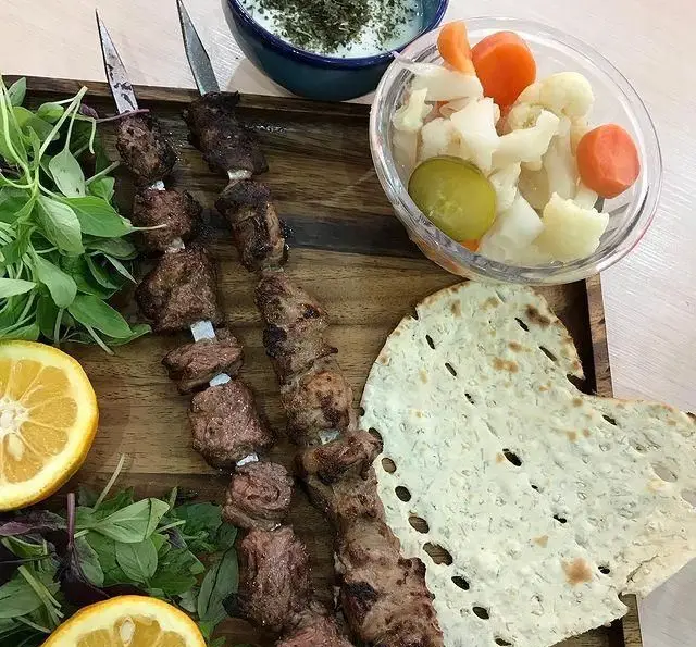تصویری جذاب از کباب دل و قلوه و جگر سیخ شده، همراه با سبزی تازه، لیمو، نان تنوری، ماست و ترشی. تجربه طعم اصیل ایرانی در جگر سرای دل و قلوه.