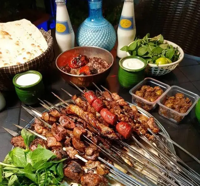 میز چیده شده با انواع کباب‌های لذیذ جگر، دل، قلوه و سوسیس کبابی از جگر سرای دل و قلوه با دوغ، نان و سبزی تازه.