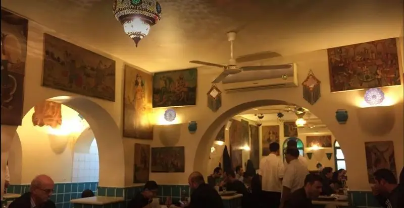 فضای داخلی دلنشین دیزی سرای 110 با دکوراسیون سنتی، نقاشی‌های دیواری جذاب، نورپردازی گرم و مشتریانی در حال صرف غذا.