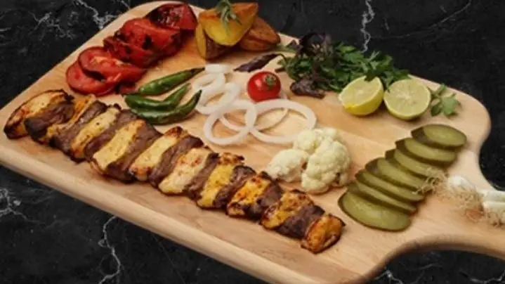 سینی کباب میکس با مخلفات تازه شامل گوجه، پیاز، لیمو، ترشی و سبزیجات از کترینگ بزرگ کیبو، یک تجربه غذای اصیل ایرانی.