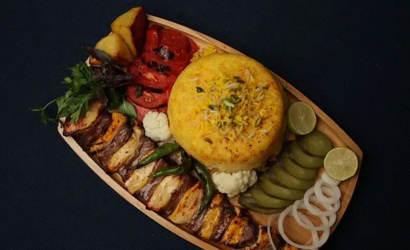 سینی غذای کترینگ بزرگ کیبو شامل کباب‌های لذیذ، چلو زعفرانی، گوجه کبابی، سیب‌زمینی و مخلفات تازه. ایده‌آل برای پذیرایی.