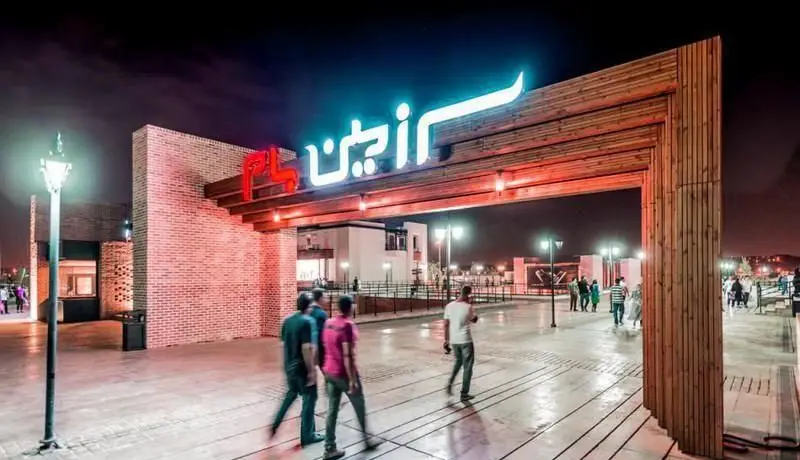 تصویری از ورودی چشم‌نواز بام لند تهران در ساعات شب، با تابلوهای نئونی و طراحی چوبی، محیطی دعوت‌کننده برای تجربه خرید و تفریح.