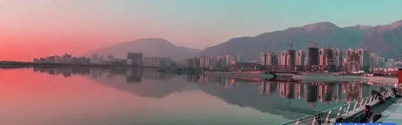 منظره چشم‌نواز پانورامیک از مجموعه تفریحی و تجاری بام لند تهران در کنار دریاچه چیتگر، با آسمان رنگارنگ غروب و انعکاس ساختمان‌ها در آب.