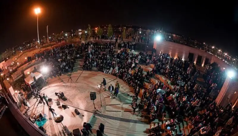 چشم‌انداز هوایی از رویداد شبانه شلوغ در بام لند تهران، نمایش حضور پرشور مردم در آمفی‌تئاتر و اجرای موسیقی زنده.