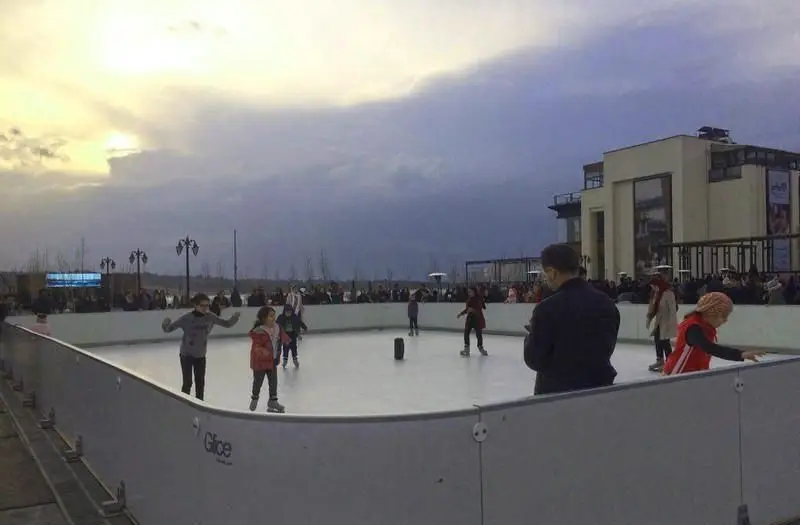 تصویری از پیست اسکیت روی یخ روباز بام لند تهران، مکانی برای تفریح خانواده و کودکان در کنار دریاچه چیتگر با آسمانی ابری.
