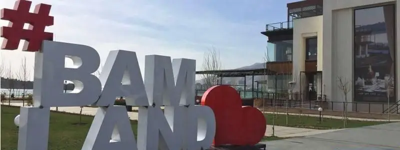 نمای بیرونی و تابلو بزرگ #بام_لند تهران با حروف سفید و قلب قرمز در کنار دریاچه، نشان‌دهنده فضای زیبای این مرکز خرید و تفریح.