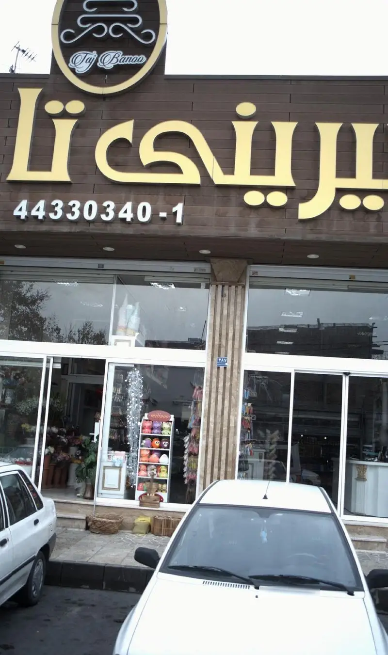 فروشگاه شیرینی و قنادی تاج بانو (Taj Banoo) با تابلو طلایی و سردر قهوه‌ای، شماره تماس 44330340-1 نمای بیرونی جذاب.