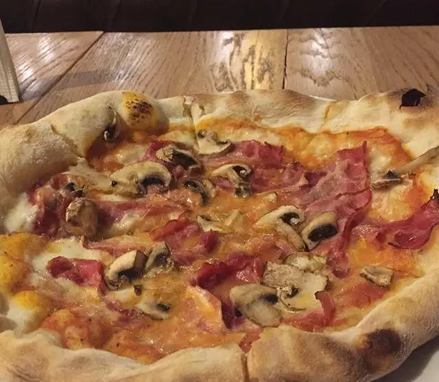 تصویری از پیتزا مخصوص کافی شاپ تیوان با نان تازه و برشته، پنیر فراوان، قارچ اسلایس شده و ژامبون لذیذ روی میز چوبی.