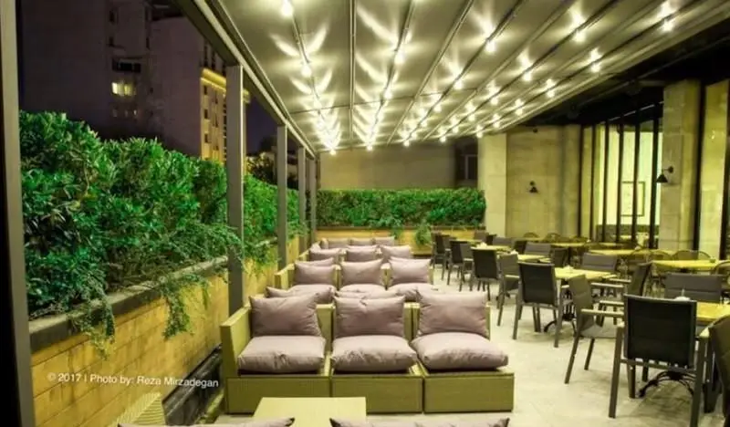 فضای باز دلنشین کافی شاپ تیوان با سقف متحرک نورپردازی شده، مبلمان راحت و فضای سبز دنج برای تجربه ای آرامش بخش در شب.