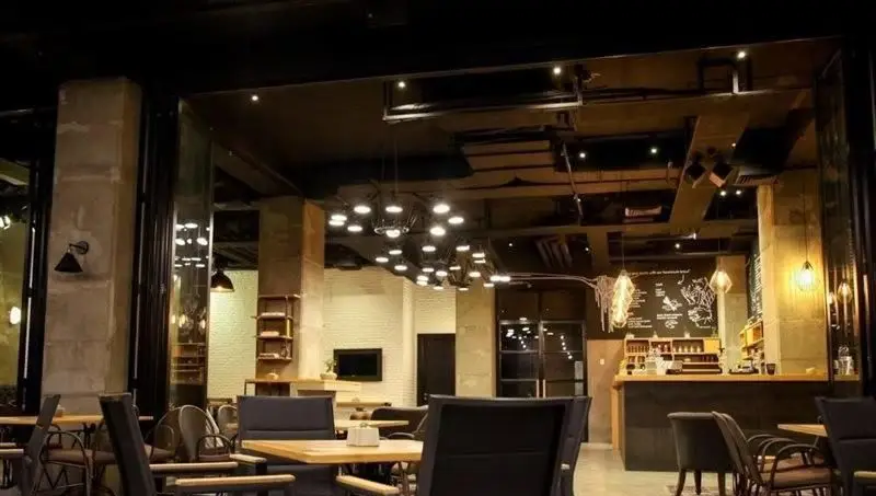 فضای داخلی مدرن و دنج کافی شاپ تیوان با طراحی صنعتی، میز و صندلی‌های راحت، نورپردازی گرم و کانتر جذاب برای سرو قهوه و نوشیدنی‌ها.