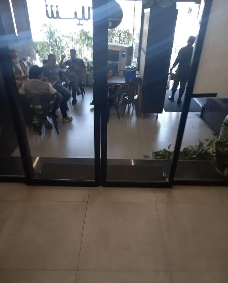 تصویری از فضای داخلی دلنشین و شلوغ کافه شیلا، شامل میز و صندلی‌ها، افراد در حال گفتگو، و درب‌های شیشه‌ای ورودی. مناسب برای کسب و کار شیلا.