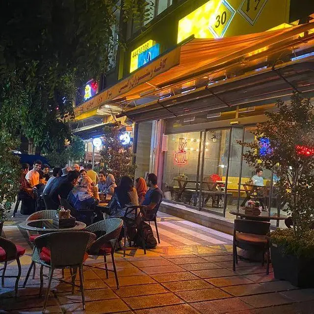 نمای شبانه از کافه رستوران و فست فود رامسی (RAMCY) با مشتریان در فضای باز و داخلی، محیطی گرم و دلپذیر.