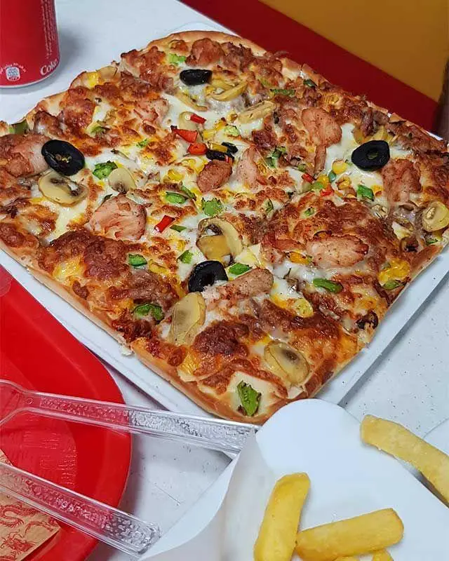 پیتزا مربع قارچ و مرغ ویژه فست فود دراگون 1 (اژدهای سرخ) با تاپینگ‌های رنگارنگ، کنار سیب‌زمینی سرخ‌کرده و نوشابه.