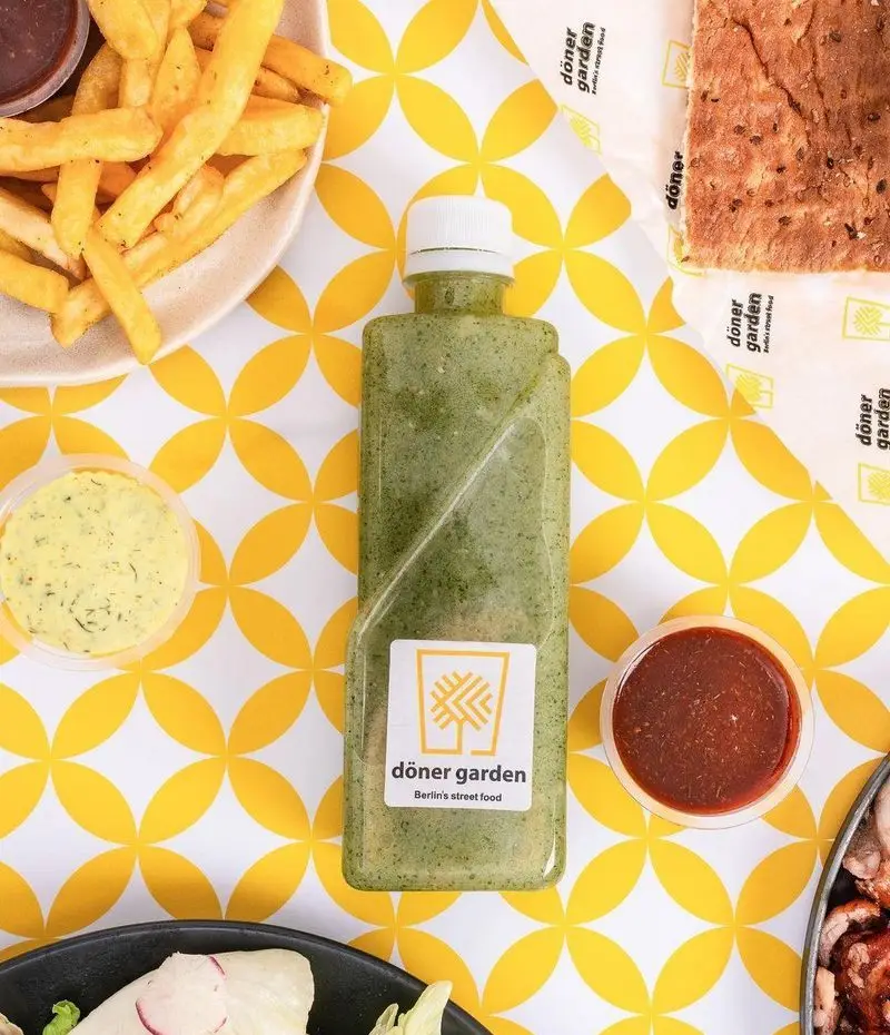 تصویر میز فست فود دونر گاردن پاسداران با سیب زمینی، سس‌های متنوع، سس سبز مخصوص بطری و بخشی از دونر. غذای خیابانی برلین.