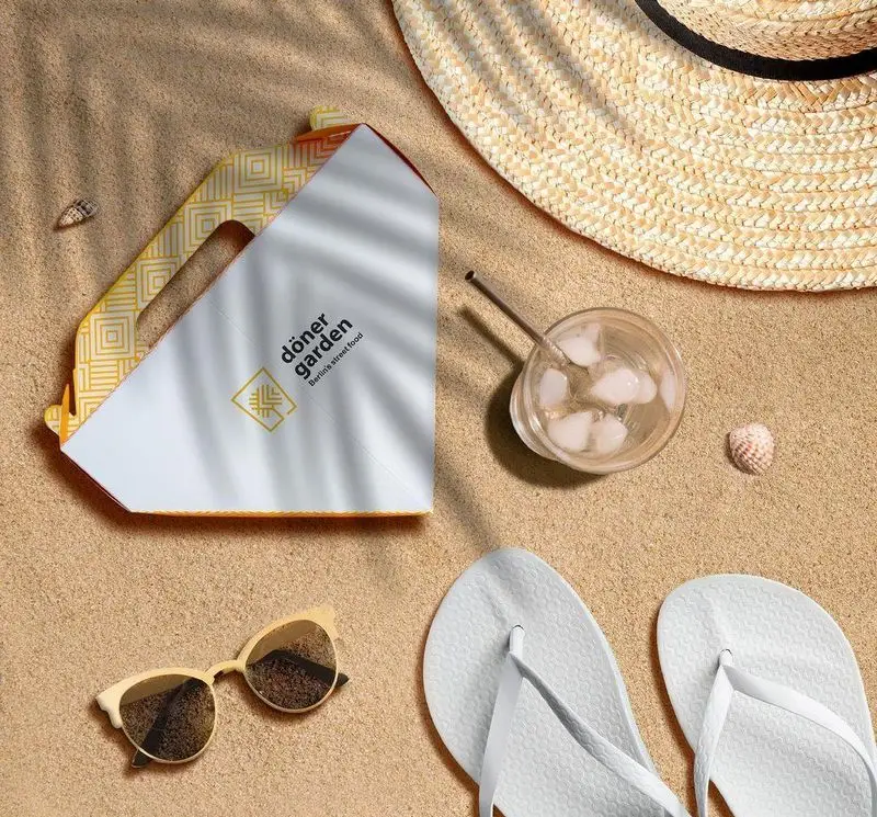 تصویر هوایی از باکس فست فود دونر گاردن پاسداران روی شن ساحل، همراه کلاه حصیری، نوشیدنی خنک، عینک و دمپایی تابستانی