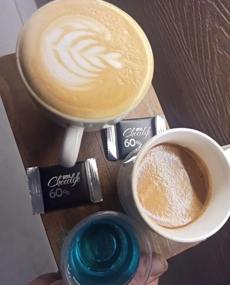 کافه نیلو: فنجان لاته با لاته آرت برگ، اسپرسو، دو شکلات چاکولایف 60% و یک نوشیدنی آبی. بهترین قهوه و دسرها در کافه نیلو.