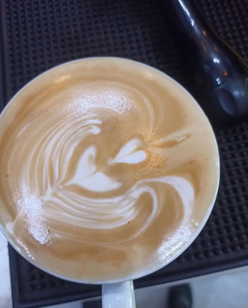 قهوه لاته آرت با طرح قلب و الگوهای زیبا، یک تجربه دلپذیر در کافه نیلو، مکانی دنج برای علاقه مندان به نوشیدنی‌های گرم.