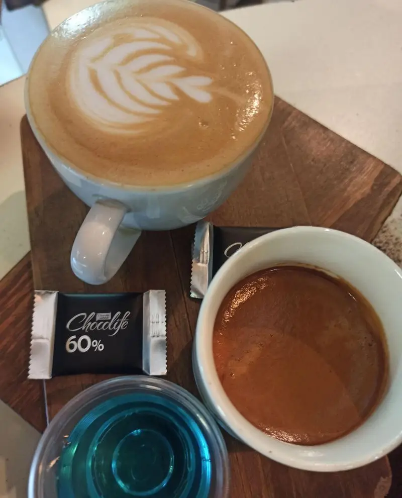 تصویری جذاب از سفارش قهوه در کافه نیلو: لاته با هنر باریستا، اسپرسو کلاسیک، شکلات تلخ ۶۰ درصد و نوشیدنی آبی خنک. تجربه‌ای دلپذیر.