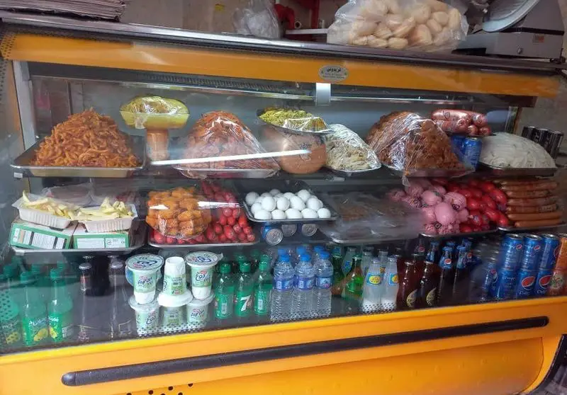 یخچال ویترینی اغذیه فروشی احد: مجموعه‌ای کامل از غذاهای آماده، فست فود، سیب زمینی سرخ کرده، ناگت، سوسیس، تخم مرغ و نوشیدنی‌های خنک