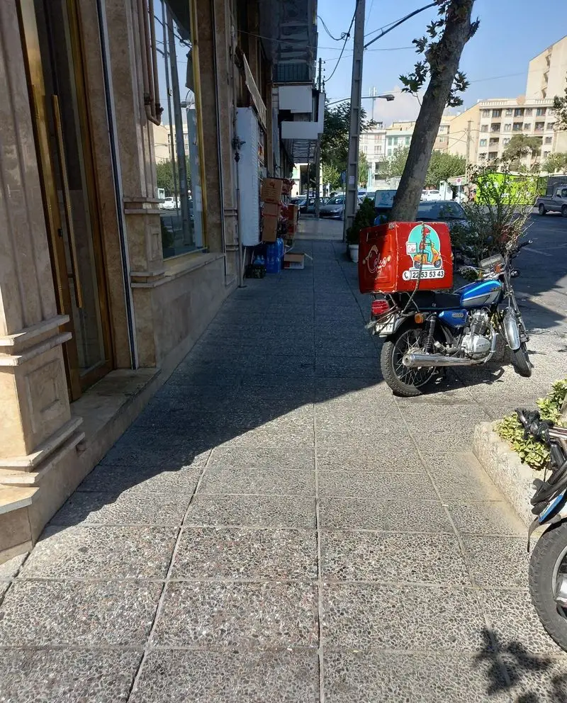 نمایی از موتور پیک آبی فست فود میلو با جعبه قرمز در خیابان، آماده برای ارسال سریع غذا و ارائه خدمات تحویل مطمئن.