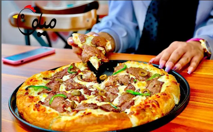 لذت بردن از پیتزا گوشت مخصوص فست فود میلو با پنیر فراوان و تاپینگ‌های تازه شامل فلفل دلمه و زیتون. یک غذای لذیذ در میلو.