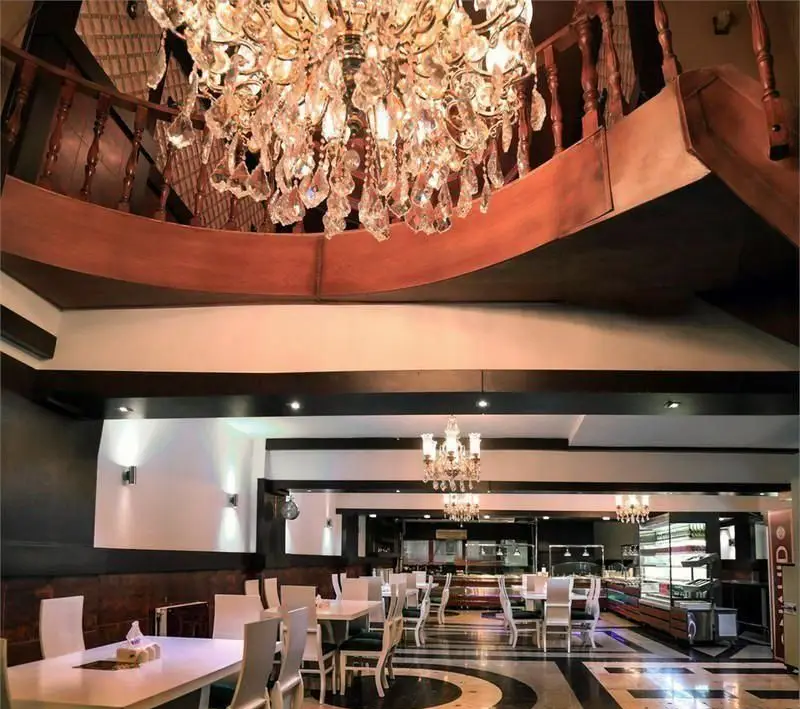 دکوراسیون داخلی لوکس و شیک رستوران ایرانی ناهید با لوستر کریستالی چشم‌نواز، پله‌های چوبی و چیدمان میز و صندلی‌های سفید مدرن.