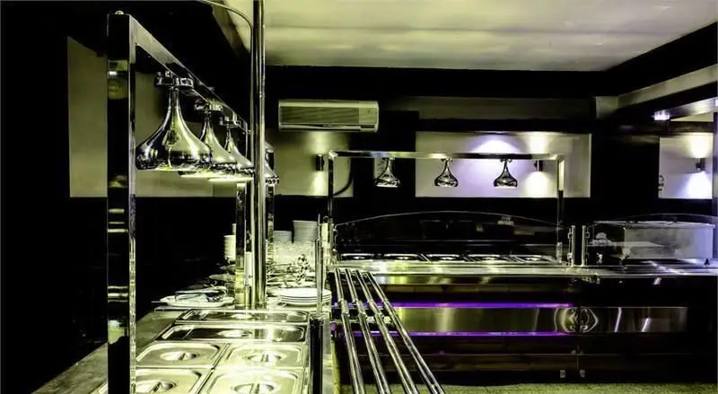 نمایی از بوفه سلف سرویس مدرن و تمیز رستوران ایرانی ناهید، مجهز به تجهیزات استیل و چراغ‌های گرم‌کننده غذا، آماده برای سرو غذای ایرانی.