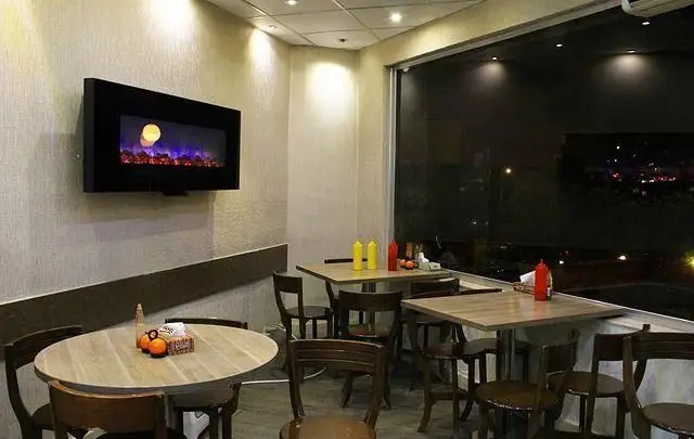 فضای داخلی دنج و مدرن رستوران پیتزا رم با میز و صندلی‌های چوبی، شومینه دیواری و پنجره‌ای رو به منظره شب شهر، ایده‌آل برای یک وعده غذایی لذیذ.