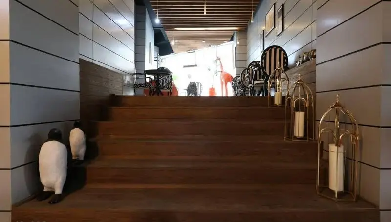 دکوراسیون داخلی کافه رستوران پلاس شیم با پله‌های چوبی، مجسمه‌های پنگوئن و فانوس‌های طلایی شمع‌دار، فضایی شیک و دلنشین.