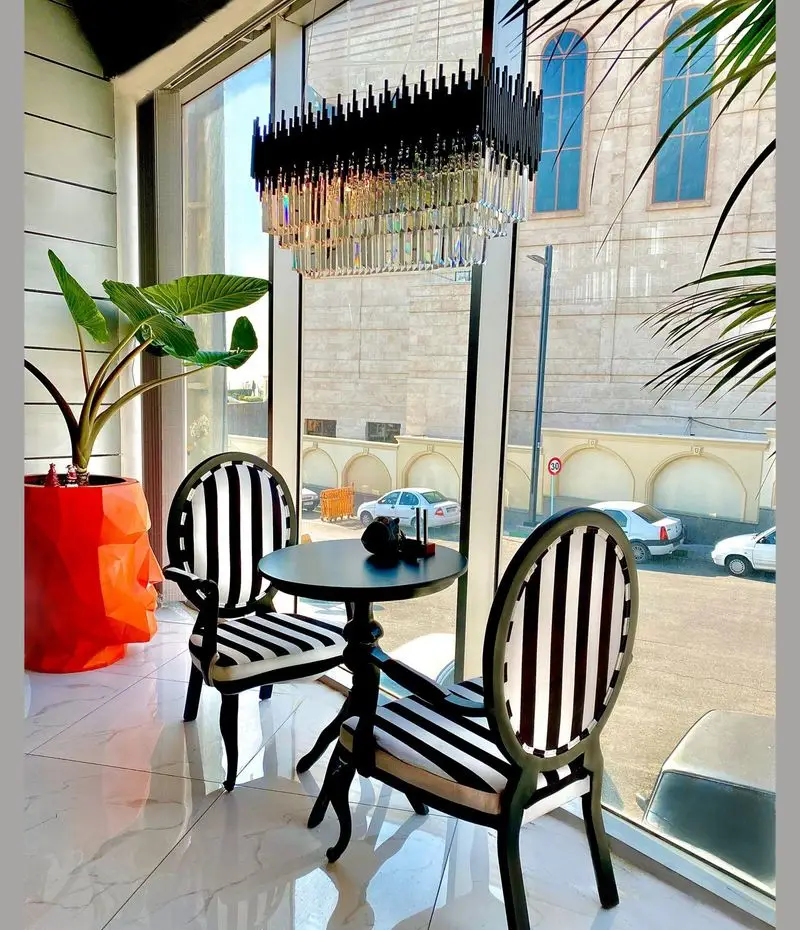 فضای داخلی لوکس کافه رستوران پلاس شیم با مبلمان مدرن سیاه و سفید، میز ناهارخوری شیک، لوستر کریستالی چشمگیر و چشم‌انداز شهری.