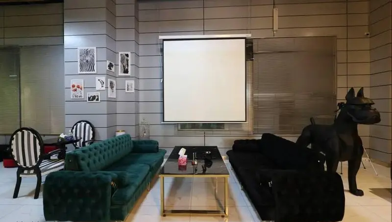 فضای داخلی لوکس و مدرن کافه رستوران پلاس شیم با چیدمان مبلمان راحتی سبز و مشکی، میز جلو مبلی، پرده نمایش و مجسمه سگ دکوری.