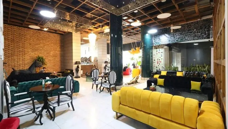 فضای داخلی شیک و مدرن کافه رستوران پلاس شیم با مبلمان زرد، سبز و سیاه، دیوار آجری، سقف چوبی و مجسمه اسب.