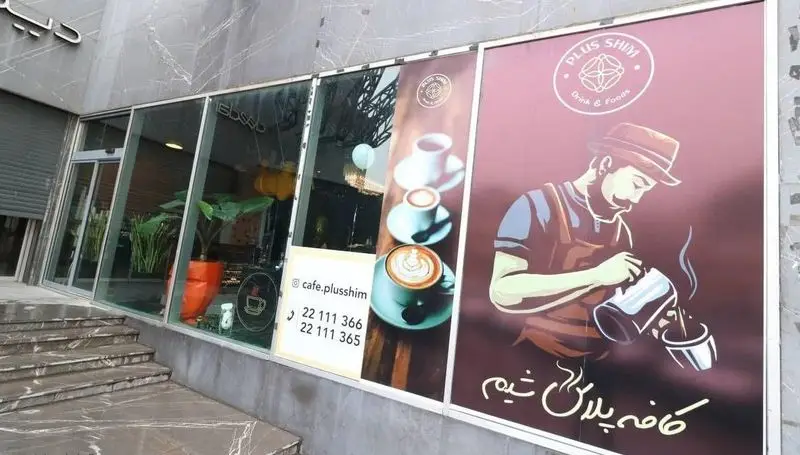 نمای بیرونی کافه رستوران پلاس شیم با تابلوی بزرگ باریستا، تصویر فنجان قهوه، شماره تماس و آدرس اینستاگرام cafe.plusshim برای سفارش آنلاین.