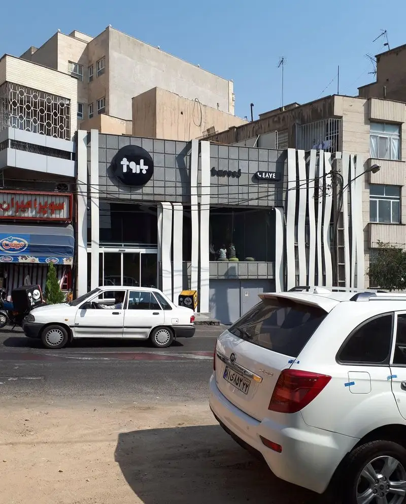 نمای بیرونی رستوران باروژ در یک روز آفتابی، با معماری مدرن شامل تابلوی گرد مشکی باروژ و نوارهای سفید عمودی روی نما.