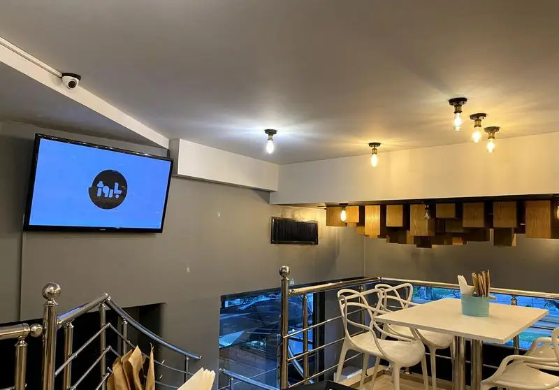 دکوراسیون داخلی مدرن رستوران باروژ شامل تلویزیون بزرگ با لوگوی باروژ، سقف با لامپ‌های روشنایی و طراحی چوبی خاص، و میز و صندلی‌های سفید.