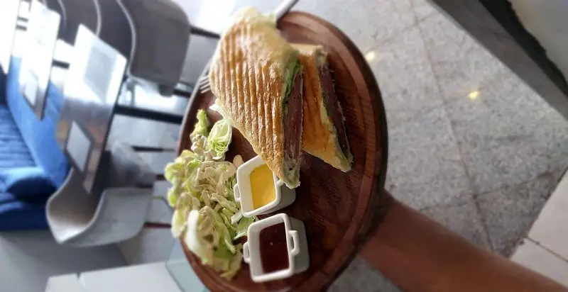 ساندویچ گریل گوشت تازه و خوشمزه، همراه با سالاد و سس‌های متنوع در سینی چوبی، سرو در کافه و رستوران تراس لانژ برای تجربه‌ای دلپذیر.