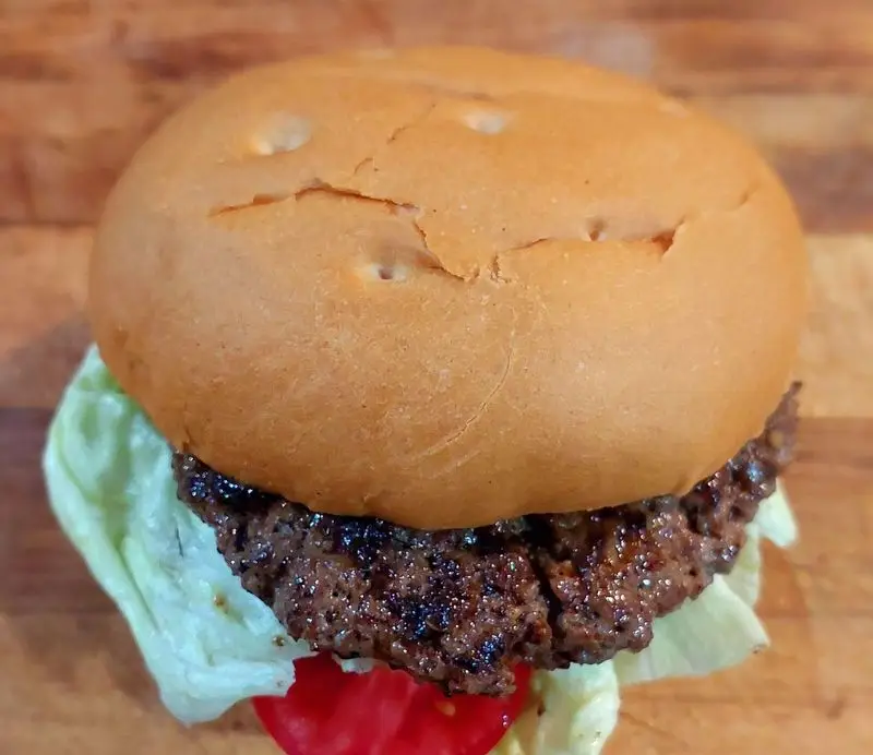 تصویر نزدیک از یک همبرگر با نان برگر طلایی، پتی گوشت گریل شده، کاهو تازه و گوجه فرنگی قرمز در کافه و رستوران تراس لانژ.